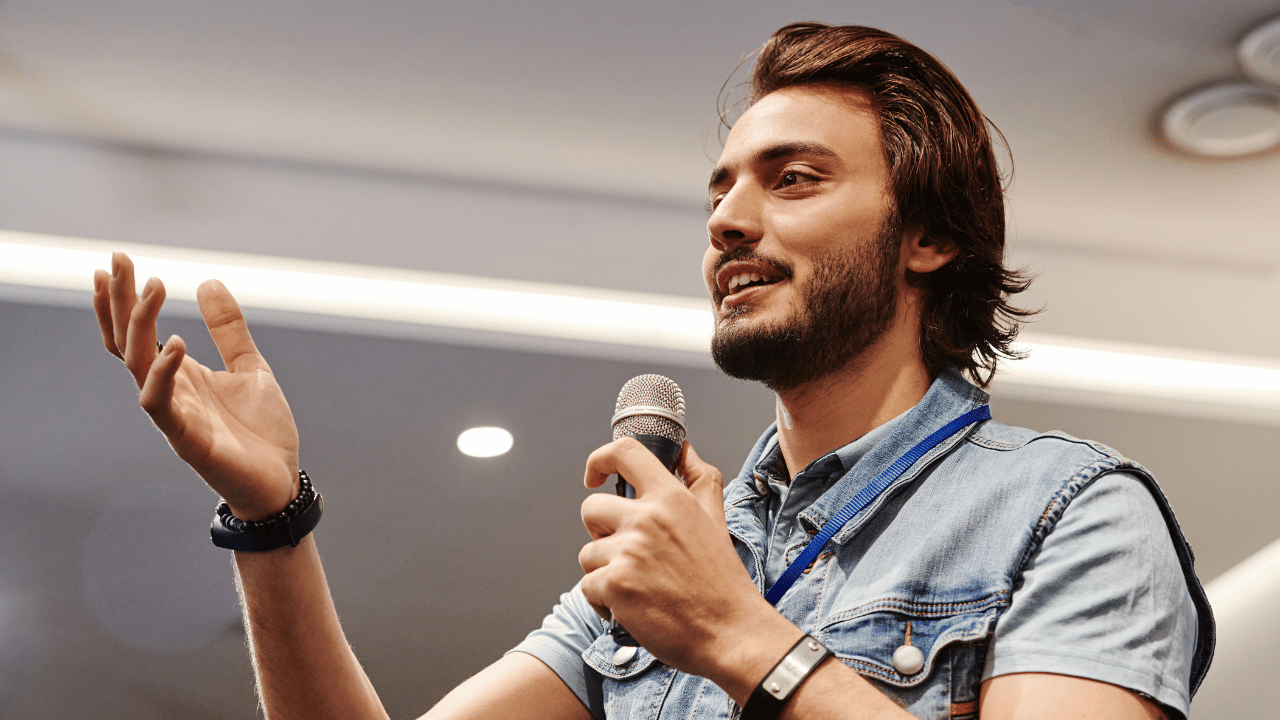 Male with long brown hair and a beard speaking into a microphone
