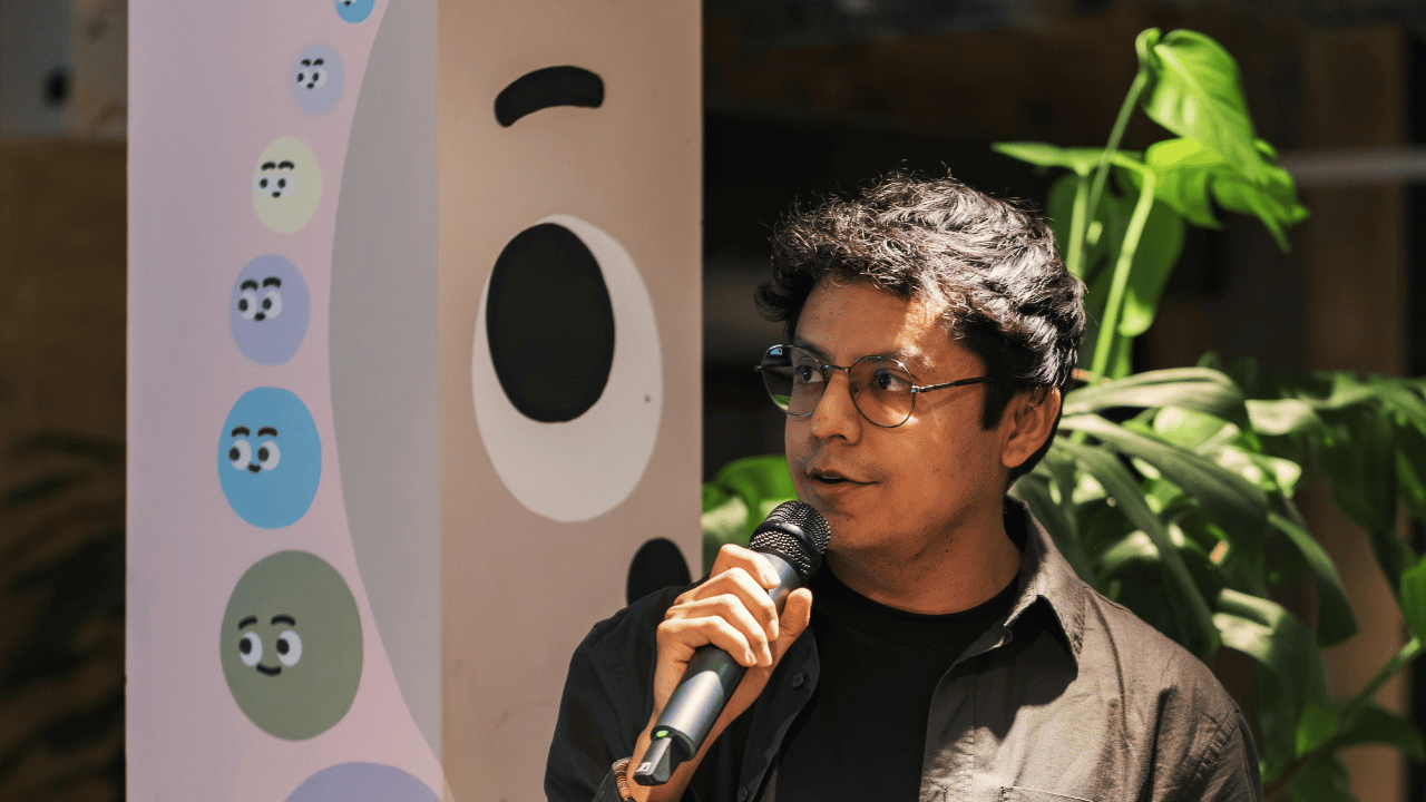 Indian man with glasses speaking into a microphone