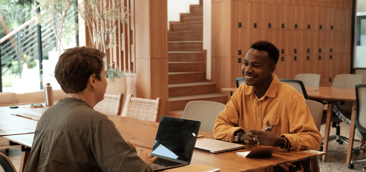 Meeting between a young black male and white female in an open plan office with timber finishes