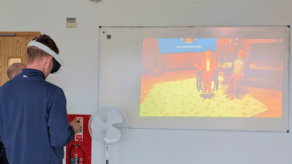 Male student with VR headset facing image projected onto wall showing Bodyswaps simulation