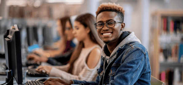 Young black male student with glasses turned to face towards the camera with a big smile on his face
