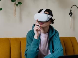 Student sitting on a yellow couch wearing a turquoise jersey, a light pink undershirt and a white VR headset